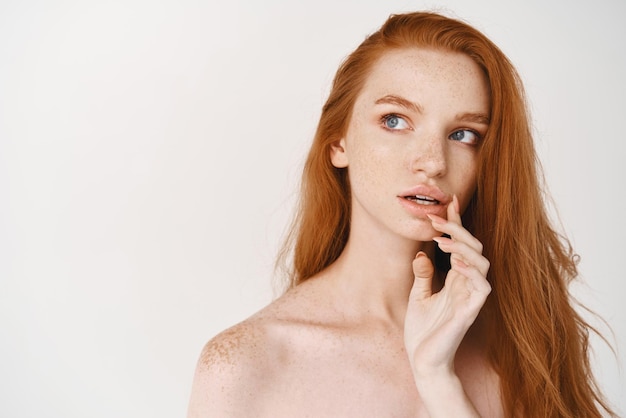 Belleza y cosmetología Primer plano de una mujer joven y hermosa con el pelo rojo largo natural y ojos azules preguntándose algo mirando la esquina superior izquierda pensando en el fondo blanco