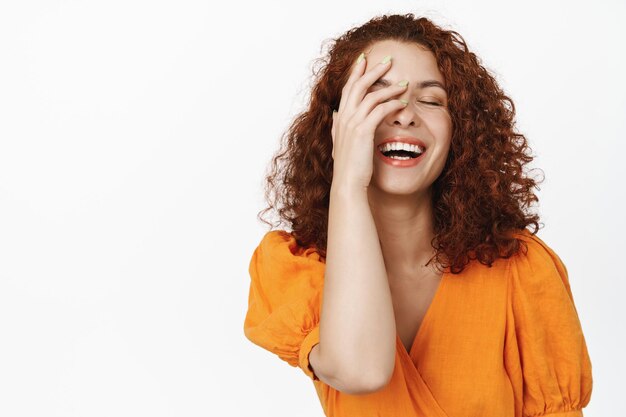 Belleza del cuidado de la piel. Modelo femenino pelirroja feliz riendo, tocando piel natural limpia sin maquillaje, riendo sinceramente, de pie sobre fondo blanco.