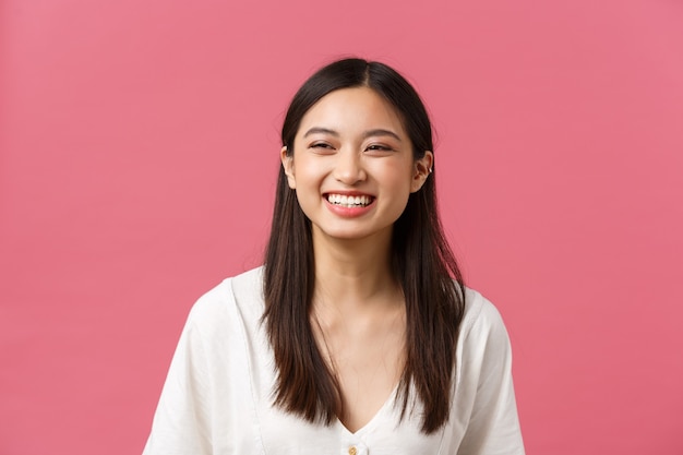 Belleza, emociones de la gente y concepto de ocio de verano. Alegre y despreocupada mujer asiática riendo disfrutando del verano, de pie fondo rosa, sonriendo alegremente, con un estado de ánimo positivo.