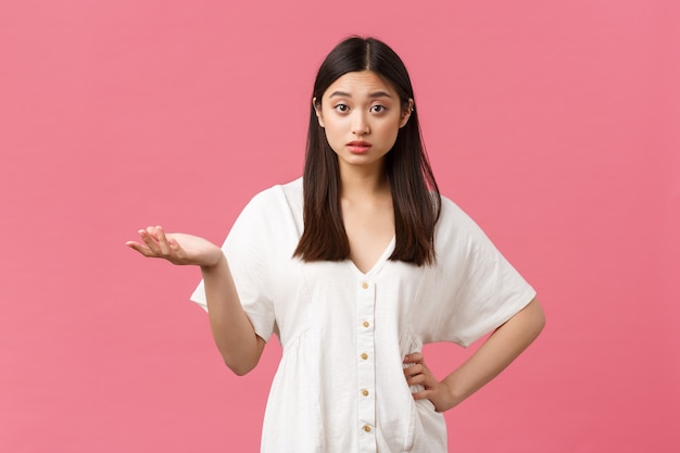 Belleza, emociones de la gente y concepto de ocio de verano. Chica asiática confundida y perpleja con vestido blanco, levantar la mano y encogerse de hombros, no puedo entender lo que quieres, fondo rosa.