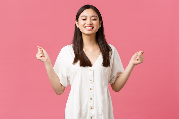 Belleza, emociones de la gente y concepto de ocio de verano. Joven confiada linda chica asiática sonriendo optimista, sintiendo fuerza y entusiasmo, aprieta las manos en puños animados y sonriendo con los ojos cerrados.