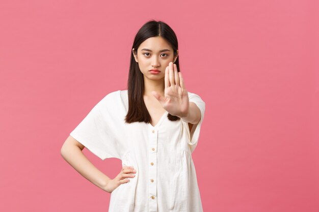 Belleza, emociones de la gente y concepto de ocio de verano. La mujer asiática joven seria y harta dice que se detenga, extienda la mano en la prohibición, dé una advertencia o restrinja el acceso denegado, fondo rosa.