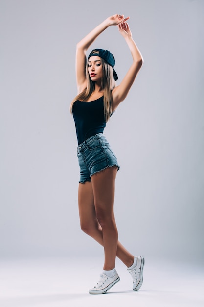 Belleza de estilo funky. Retrato de hermosa mujer joven con gafas y sombrero funky mientras está de pie contra la pared gris