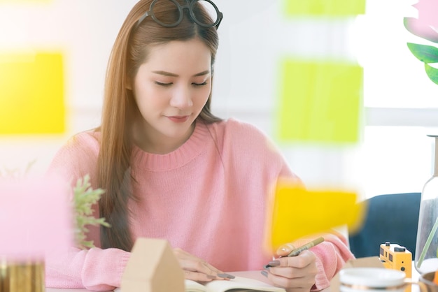 Belleza inteligente mujer asiática vestido de color rosa trabajo informal en casa con una nota de papel adhesiva y una reunión de documentos de datos consultar en la mesa de reuniones