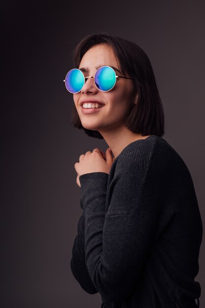 Belleza Moda modelo joven morena con gafas de sol con estilo aislados en gris. Blogger de moda