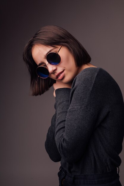 Belleza Moda modelo joven morena con gafas de sol con estilo aislados en gris. Blogger de moda