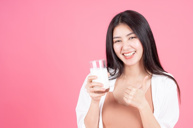 Belleza de la mujer asiática linda niña siente feliz bebiendo leche para una buena salud en la mañana sobre fondo rosa