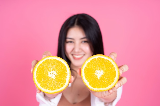 Belleza de la mujer asiática linda niña siente feliz holdind fruta naranja para una buena salud sobre fondo rosa