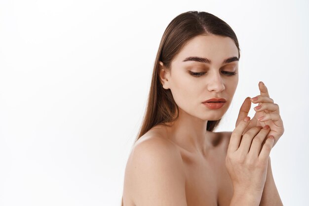 Belleza y spa. Mujer femenina sin maquillaje natural, piel limpia hidratada, efecto hidratante, mirando hacia abajo con mirada sensual, mostrando manos, crema de manos o anuncio de cosmetología