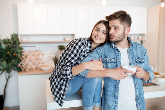 Besar a joven feliz y mujer en la cocina, desayuno, pareja juntos en la mañana, sonriendo, tomando té