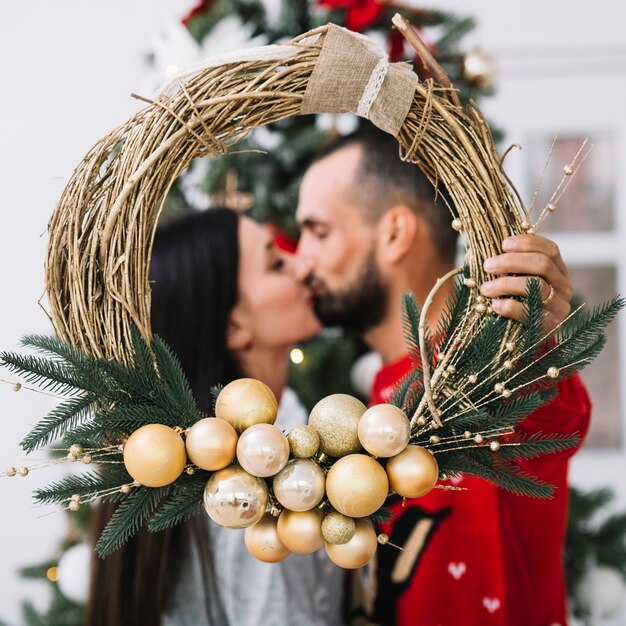 Beso hombre y mujer con corona de navidad.