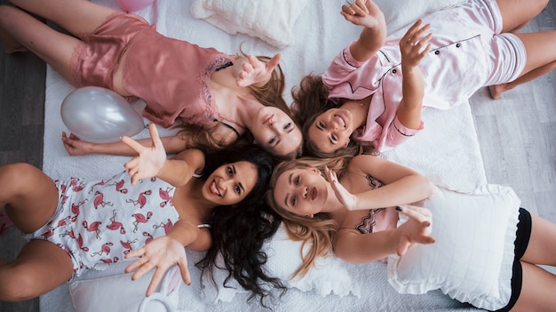 Besos al aire. Vista superior de chicas jóvenes en despedida de soltera tumbada en el sofá y levantando las manos