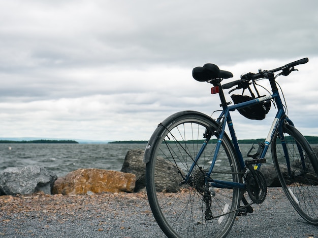 Bicicleta de montaña azul estacionada en la orilla del mar bajo un cielo nublado