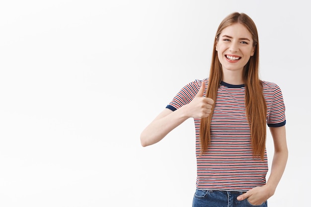 Foto gratuita bien hecho, buen trabajo chica animándote a hacer un esfuerzo increíble de pie casualmente, sonríe alegremente y levanta el pulgar como una idea, sonriendo aceptando, da aprobación posando fondo blanco