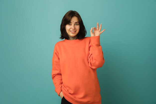 Bien, ok. Retrato de mujer caucásica aislado en la pared azul con copyspace. Modelo de mujer hermosa en sudadera con capucha naranja. Concepto de emociones humanas, expresión facial.