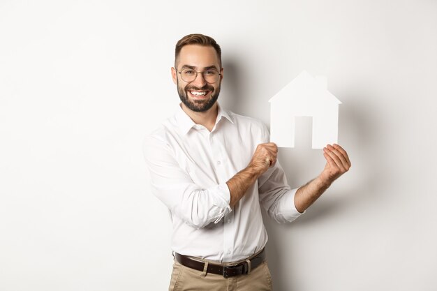 Bienes raíces. Hombre guapo mostrando modelo de casa y sonriendo, corredor mostrando apartamentos, de pie