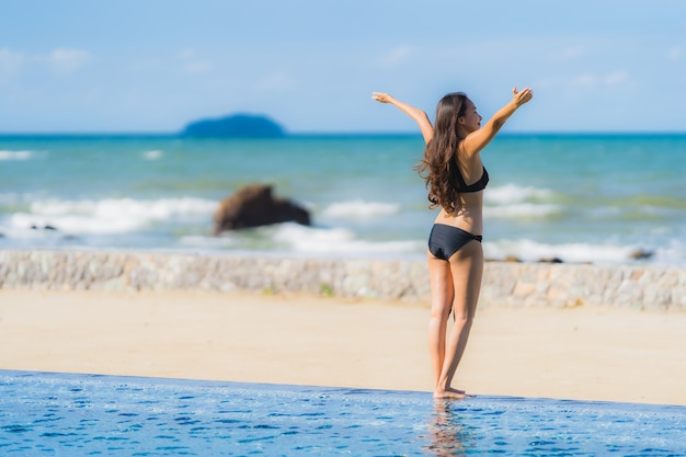 Bikini asiático hermoso joven del desgaste de la mujer del retrato alrededor de piscina en playa del océano del océano del centro turístico del hotel casi