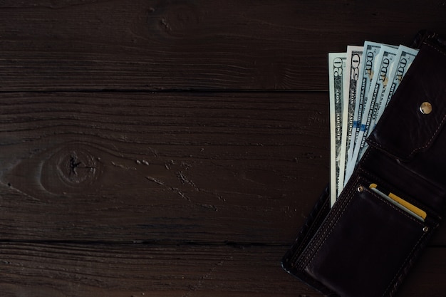 Billetes de dólar en la billetera de cuero de los hombres en la mesa de madera marrón