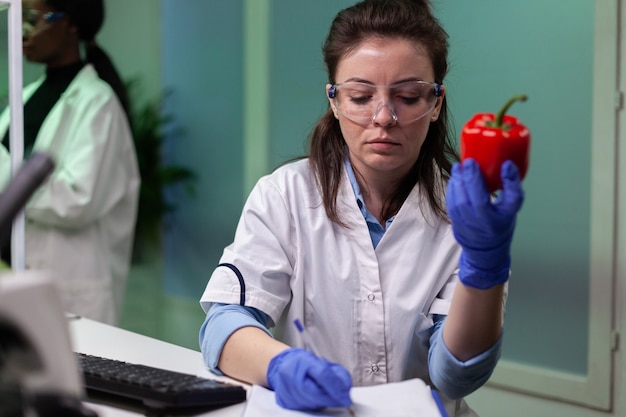 Biólogo mujer sosteniendo pimienta gmo escribiendo experiencia médica en microbiología