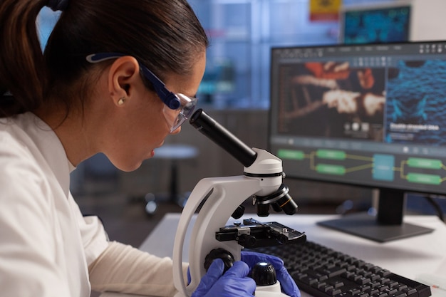 Bioquímico que trabaja en el microscopio para la ilustración celular en la pantalla de la computadora en el laboratorio químico. Mujer científica analizando adn del virus, tejido celular, diagrama de núcleo de plasma y hemoglobina