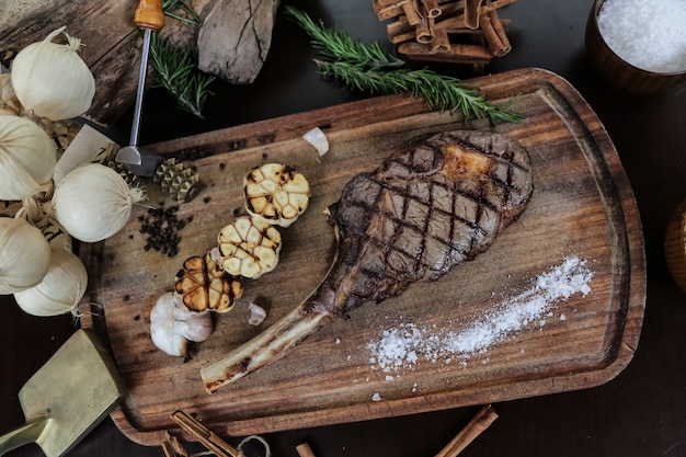 Bistec a la parrilla en la tabla de madera ajo sal romero