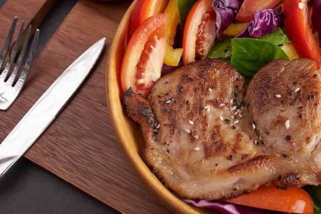 Bistec a la parrilla con verdura fresca, pimiento dulce, tomate, cebolla morada, pimiento rosa y especias. Comida sabrosa casera. Concepto de comida sabrosa y saludable. Superficie de piedra negra. Filete de cerdo con ensalada