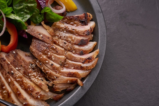 Bistec a la parrilla con verdura fresca, pimiento dulce, tomate, cebolla morada, pimiento rosa y especias. Comida sabrosa casera. Concepto de comida sabrosa y saludable. Superficie de piedra negra. Filete de cerdo con ensalada