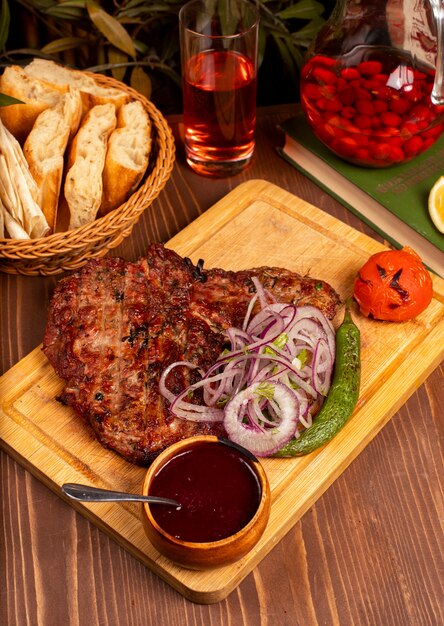 Bistec de ternera con barbacoa, salsa barbacoa y hierbas, ensalada de cebolla, pimiento asado y tomate en un plato de madera