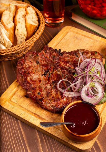 Bistec de ternera con barbacoa, salsa barbacoa y hierbas, ensalada de cebolla, pimiento asado y tomate en un plato de madera