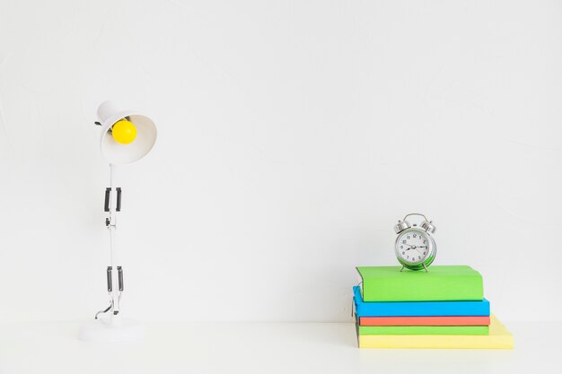 Blanco espacioso lugar de trabajo con coloridos cuadernos y reloj despertador