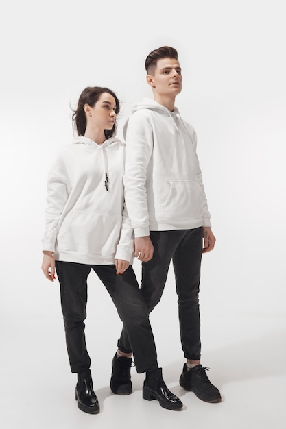 En blanco. Pareja de moda de moda aislada en la pared blanca. Mujer caucásica y hombre posando en ropa unisex mínima básica. Concepto de relaciones, moda, belleza, amor. Inclusivo.