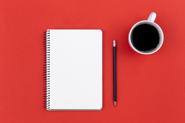 Bloc de notas en blanco taza de café y lápiz sobre fondo rojo endecha plana