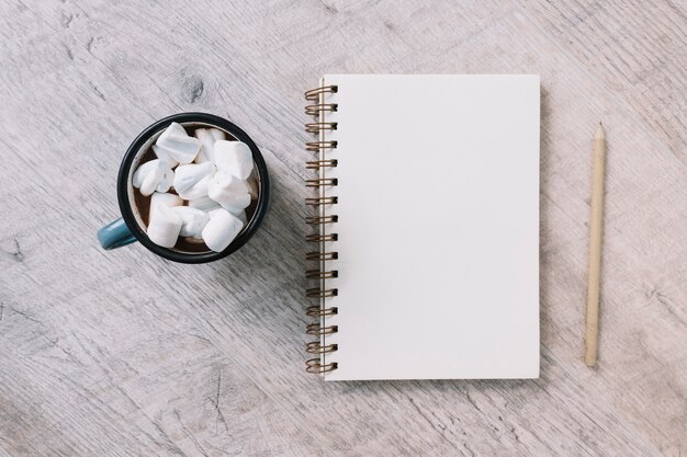 Bloc de notas en blanco con taza de malvaviscos