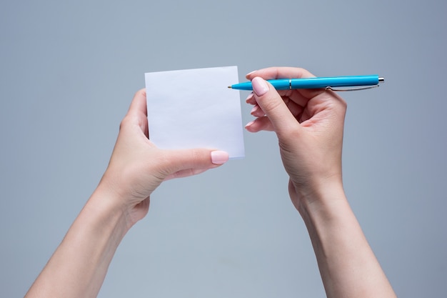 El bloc de notas y el bolígrafo en manos femeninas sobre fondo gris