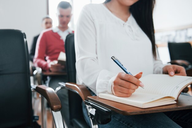 Con bloc de notas y bolígrafo en las manos. Grupo de personas en conferencia de negocios en el aula moderna durante el día