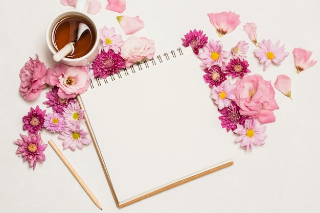 Bloc de notas cerca de conjunto de flores y taza de bebida