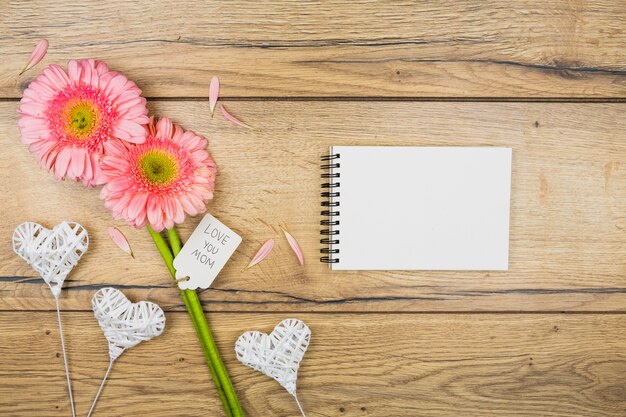 Bloc de notas cerca de flores frescas con etiqueta cerca de corazones ornamentales en varitas