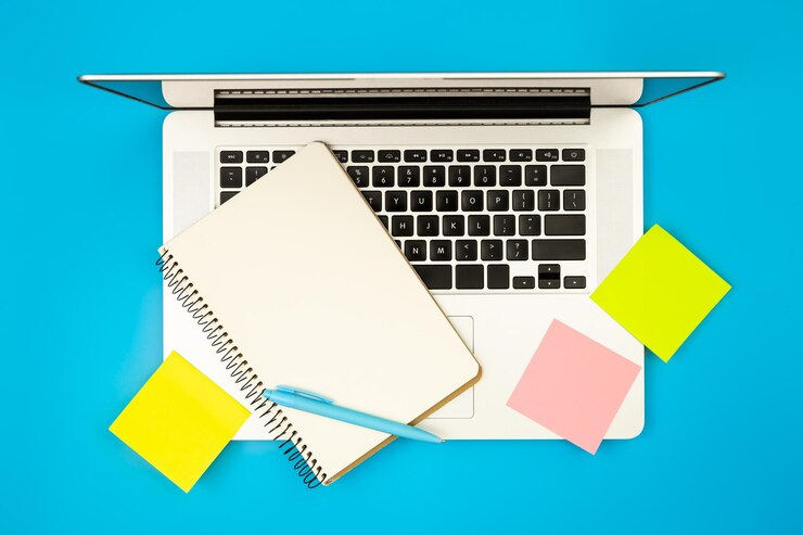 Foto gratuito el bloc de notas de la computadora portátil y los recordatorios de papel en un fondo azul plano