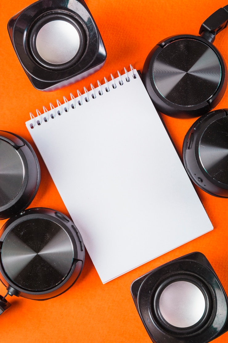 Foto gratuito bloc de notas de espiral blanco en blanco con auriculares y altavoz sobre un fondo naranja