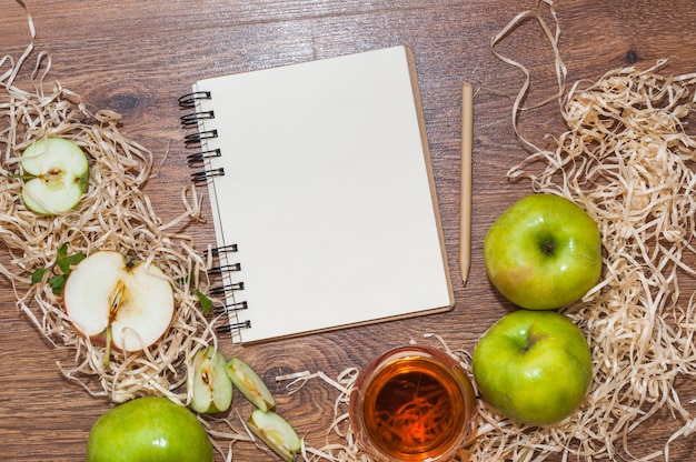 Foto gratuita bloc de notas de espiral en blanco; lápiz y manzana verde con vinagre de manzana en el escritorio de madera