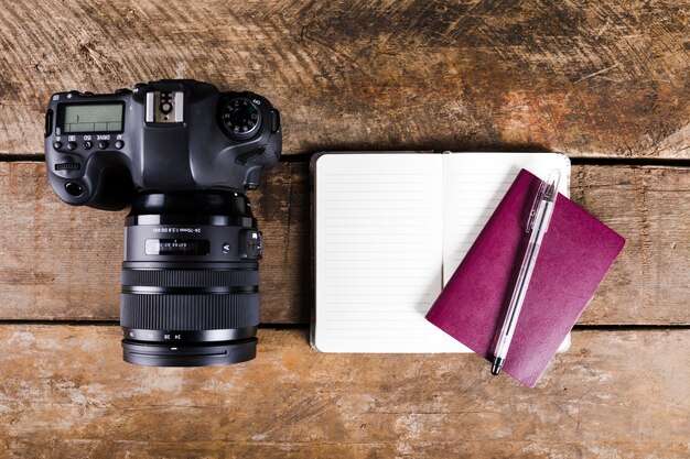 Bloc de notas, pasaporte, pluma y cámara DSLR sobre fondo de madera