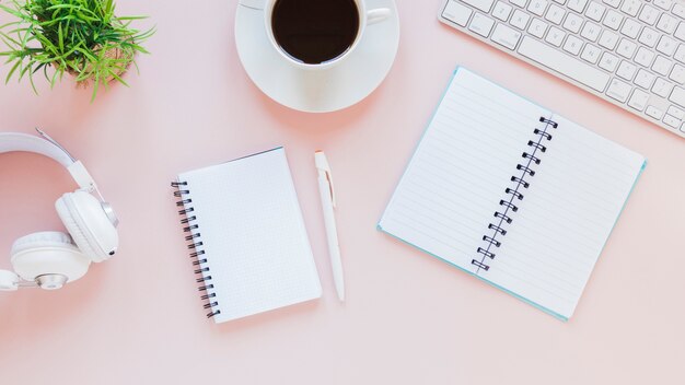 Blocs de notas y taza de café cerca de auriculares y teclado