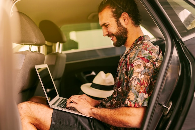 Blogger alegre usando laptop en auto