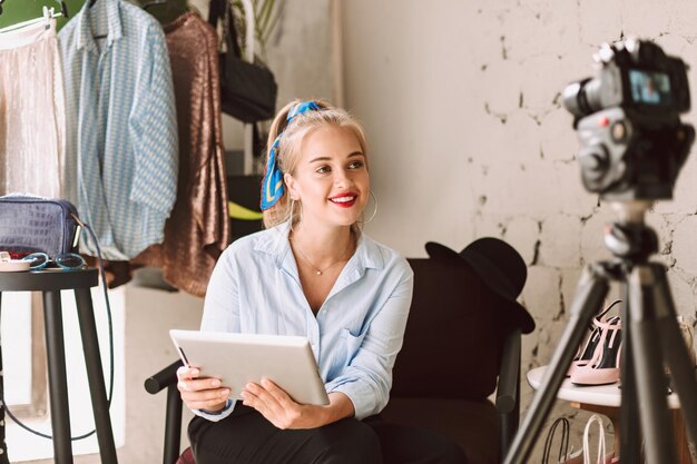 Blogger de belleza sonriente usando la tableta mientras graba felizmente un nuevo video de moda para vlog en cámara