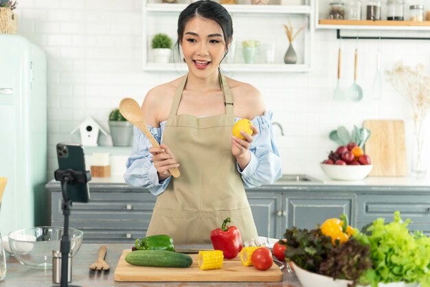 Blogger de comida asiática cocinando ensalada frente a la cámara del teléfono inteligente mientras graba video vlog