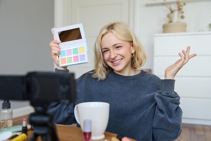 Foto gratuito blogger de estilo de vida graba video en su habitación tiene una cámara en la mesa de café muestra la paleta de sombra de ojos a