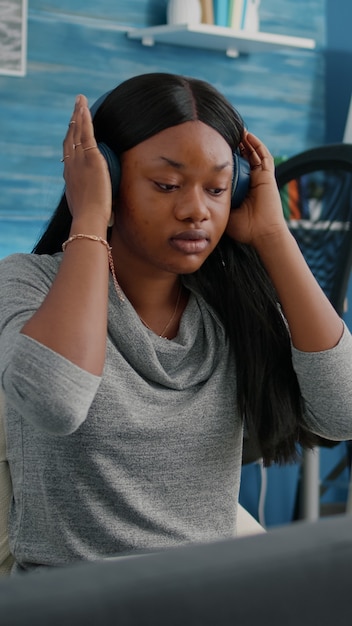 Blogger estudiante afroamericano poniendo auriculares trabajando de forma remota desde casa