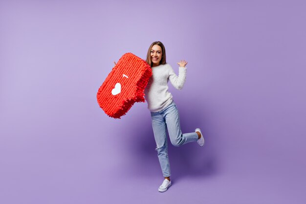 Blogger femenina de buen humor bailando con una sonrisa. Retrato interior de una dama increíble en suéter blanco que expresa emociones felices.