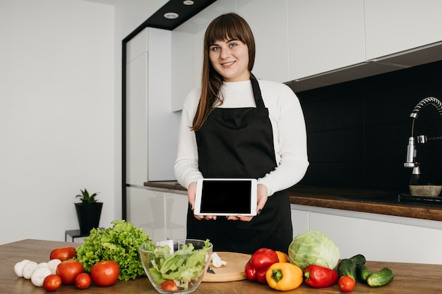 Blogger femenina grabando a sí misma mientras prepara ensalada con tableta