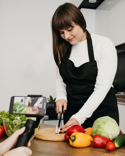 Blogger femenina grabando a sí misma mientras prepara ensalada con verduras